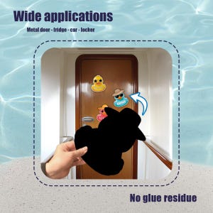 Puede incluir: Una mano sosteniendo un im&aacute;n negro con forma de pato, con el texto "Wide applications" y "No glue residue". Varios imanes de pato est&aacute;n adheridos a una puerta de madera. Los imanes tienen varios dise&ntilde;os.