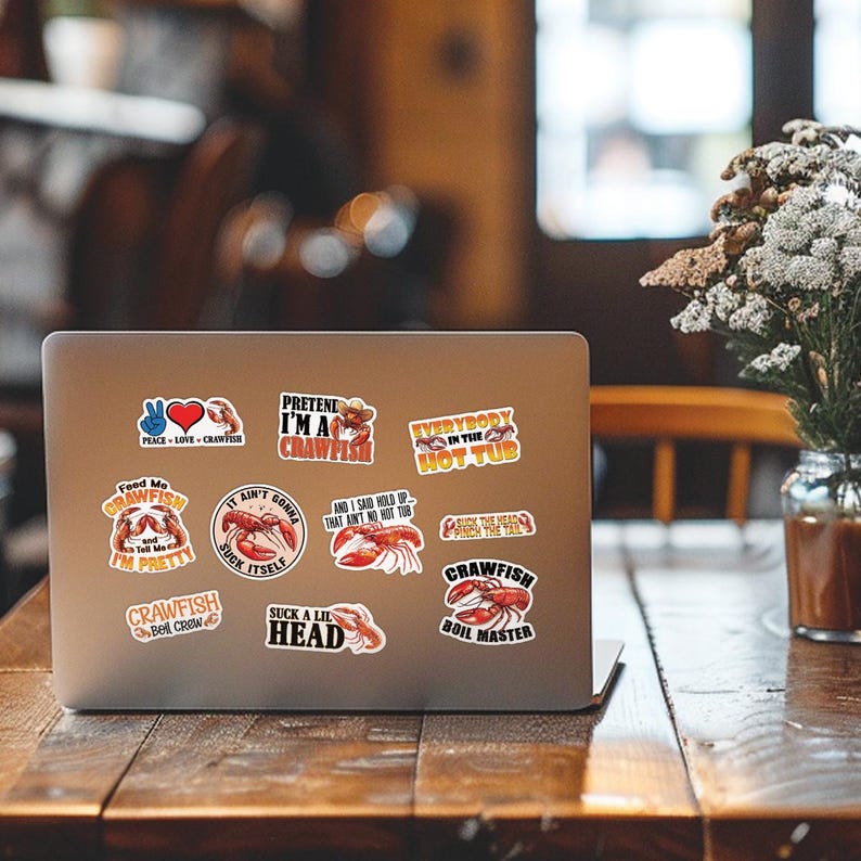 May include: A laptop computer with a variety of crawfish-themed stickers. The stickers feature crawfish illustrations and humorous sayings like "Pretend I'm a Crawfish", "Everybody in the Hot Tub", and "Crawfish Boil Master".