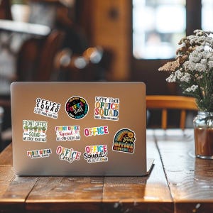 May include: A laptop computer with a variety of colorful stickers featuring office-themed sayings. The stickers include phrases like "Office Squad", "Office Crew", and "Front Office Superhero".