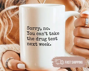 May include: White ceramic mug with the text "Sorry, no. You can't take the drug test next week." The mug has a white handle and is held by a person. The mug is a standard size.