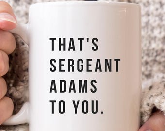 May include: A white ceramic mug featuring the black printed text THAT'S SERGEANT ADAMS TO YOU. The mug has a standard handle and a smooth, cylindrical body, providing a clear view of the bold, sans-serif lettering centered on the front surface.