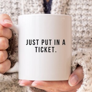 Könnte beinhalten: Eine weiße Keramik-Kaffeetasse mit schwarzem Text, der "JUST PUT IN A TICKET." lautet.