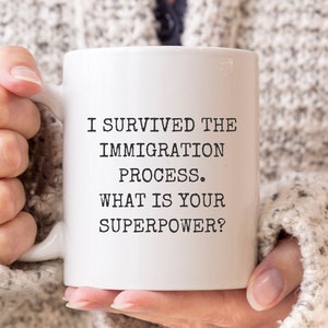 May include: White ceramic coffee mug with black text that reads "I survived the immigration process. What is your superpower?"