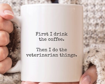 May include: White ceramic coffee mug with black text that reads "First I drink the coffee. Then I do the veterinarian things."