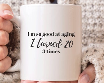 May include: White ceramic coffee mug with black text that reads "I'm so good at aging I turned 20 3 times".