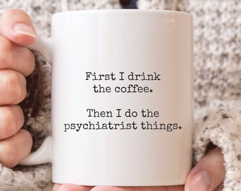 May include: White ceramic coffee mug with black text that reads "First I drink the coffee. Then I do the psychiatrist things."