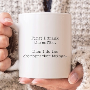 May include: White ceramic coffee mug with black text that reads "First I drink the coffee. Then I do the chiropractor things."
