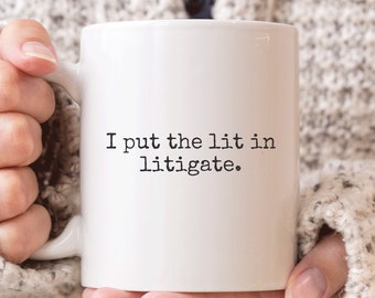 May include: White coffee mug with black text that reads "I put the lit in litigate."