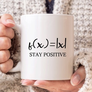 May include: White ceramic mug with black text that reads "f(x)=|x| STAY POSITIVE".