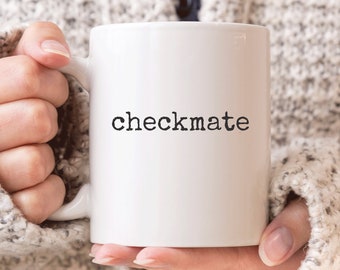 May include: White ceramic mug with the word "checkmate" printed in black.