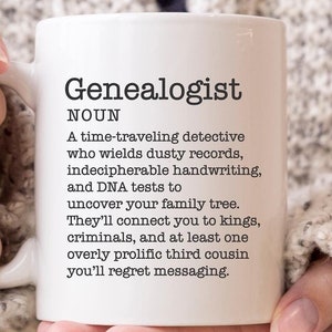 May include: White ceramic mug with a black and white definition of the word "Genealogist". The definition reads: "A time-traveling detective who wields dusty records, indecipherable handwriting, and DNA tests to uncover your family tree. They'll connect you to kings, criminals, and at least one overly prolific third cousin you'll regret messaging."