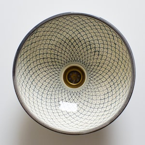 Puede incluir: Un lavabo de cerámica blanca con un patrón geométrico blanco y negro y un desagüe de latón.