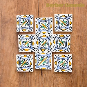 May include: Nine square ceramic tiles with a blue, white, yellow, and green floral pattern. The tiles are arranged in a grid pattern.