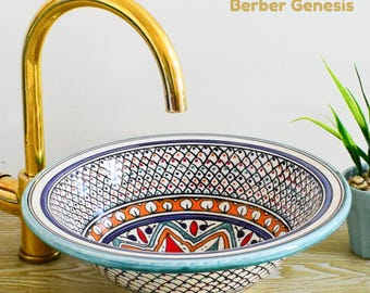 May include: A white ceramic sink with a blue, orange, and red geometric pattern. The sink is round and has a wide rim. The sink is sitting on a wooden surface. The text "Berber Genesis" is visible in the top right corner of the image.