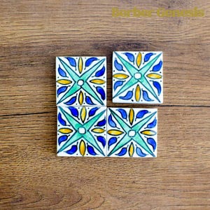 Puede incluir: Cuatro azulejos cuadrados de cerámica con un patrón geométrico azul, verde y amarillo. Los azulejos están dispuestos en una cuadrícula de dos por dos.