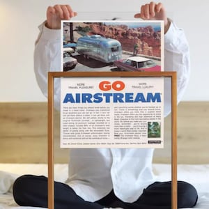 Peut inclure: Une publicité vintage pour les caravanes Airstream. La publicité présente une caravane Airstream argentée garée dans un paysage pittoresque avec une voiture rouge derrière elle. Le texte dit "Go Airstream! Plus de plaisir de voyage! Plus de luxe de voyage!"