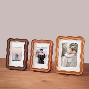 May include: Three wooden photo frames with a wavy edge design. The frames are in shades of brown and have white mounts. Each frame holds a photograph. The frames are displayed on a wooden surface.