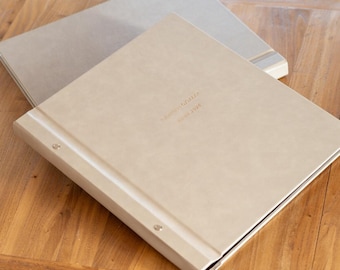 May include: Two beige photo albums with silver rings and a gold embossed inscription on the top album that reads "[Name] & [Name]  [Date]"
