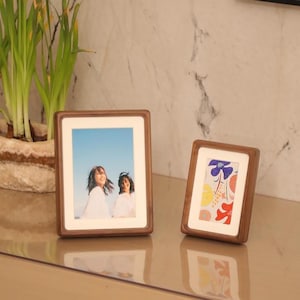 May include: Two wooden picture frames, one with a photo of two women smiling and the other with a colorful abstract design.