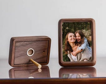 May include: Two wooden picture frames. One frame holds a photo of a woman and a child. The other frame is a wooden box with a brass rod and a circular opening. The frames are made of dark wood and sit on a reflective surface.
