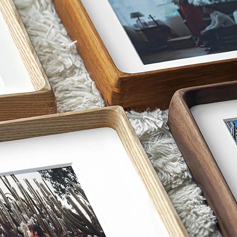 Close-up of overlapping rounded-corner solid wood picture frames in light ash, warm teak, and dark walnut tones, showing natural grain and white mats.