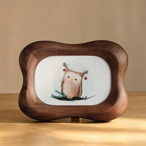 May include: A wooden picture frame with a whimsical illustration of an owl decorated with berries. The frame has a dark brown finish and a unique, curved shape. The owl is perched on a branch, adding a touch of nature to the design.