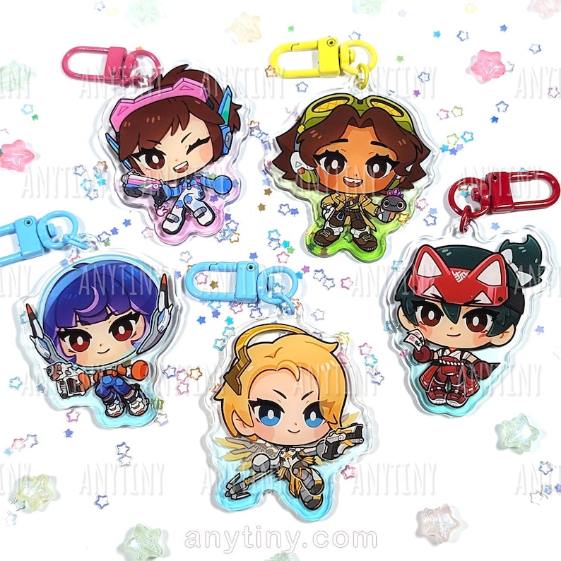 May include: Five acrylic keychains featuring cartoon characters with various hair colors and outfits. Each keychain has a different character design and a colored clasp. The keychains are on a white surface with star-shaped confetti.