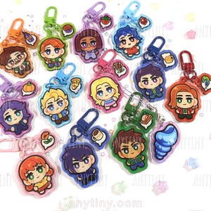 May include: A collection of colorful acrylic keychains featuring cartoon characters. Each keychain has a unique design, including characters with different hair colors and outfits, and small charms like food items. The keychains are attached to metal clasps.