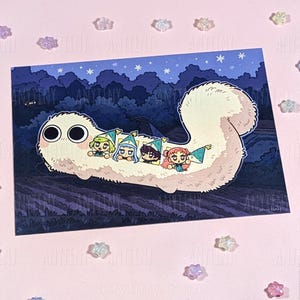 May include: A rectangular art print featuring a large, fluffy, cream-colored creature with two oversized black eyes. Four small characters wearing pointed blue hats are nestled along its back against a dark blue night sky with trees and stars.