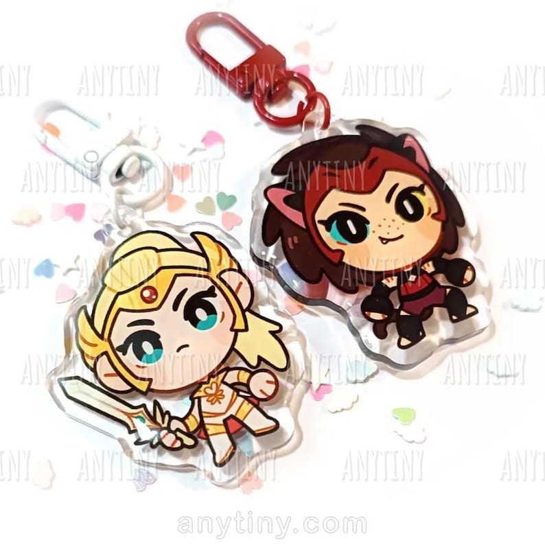 May include: Two acrylic keychains featuring cartoon characters. One keychain depicts a blonde character in gold armor holding a sword. The other keychain shows a character with brown hair and a red outfit. Both have a clear border and a red clasp.