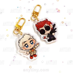 May include: Two acrylic keychains with gold-coloured clasps. One keychain features a cartoon character with red hair, sunglasses, and a glass of wine. The other keychain has a cartoon character with blonde hair and a cup. The website anytiny.com is visible.