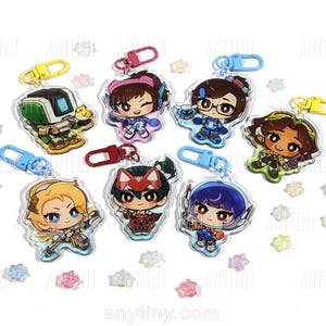 May include: A collection of seven acrylic keychains featuring chibi-style characters and a robot, each attached to a colorful plastic lobster clasp. The designs include various figures with distinct outfits and accessories, scattered among small star-shaped beads.
