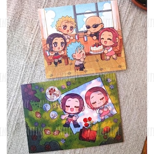 May include: Two illustrated cards featuring anime-style characters. One card depicts a group around a table with a cake, the other shows two characters on a picnic blanket with food and flowers. The cards have a cute, colorful design.