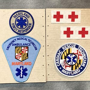 May include: A collection of embroidered patches featuring emergency medical service and first responder themes. Includes patches with the Maryland state flag, the Star of Life, and the words "Maryland", "First Responder", "Emergency Medical Technician", and "Cardiac Rescue Technician".