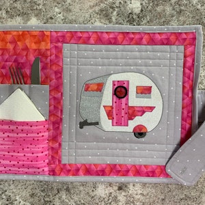 Puede incluir: Un mantel individual acolchado gris y rosa con un bolsillo para cubiertos y una servilleta. El mantel individual presenta un diseño de autocaravana rosa y blanco.