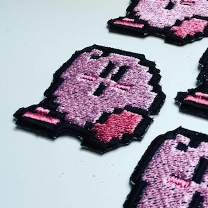 Peut inclure: Quatre patchs brodés roses et noirs du personnage de jeu vidéo Kirby. Chaque patch représente Kirby avec un blush rose et un cœur rose.