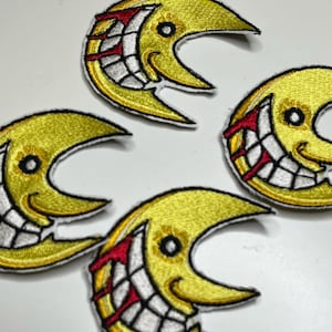 Op de afbeelding: Vier gele halve maan patches met een witte, tandenrijke grijns en rood druppend bloed. De patches zijn geborduurd met witte en rode draad.
