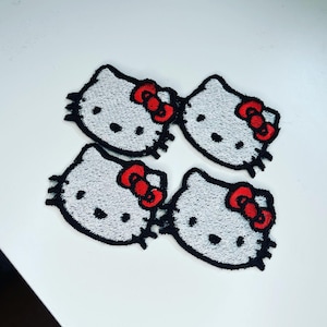 May include: Four white embroidered iron-on patches of Hello Kitty with red bows.