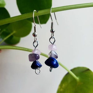 May include: Dangle earrings with natural gemstones. Each earring has a silver hook and three stones: dark blue, purple, and light pink. The earrings are displayed against a green background. The gemstones are likely to be measured in millimetres.
