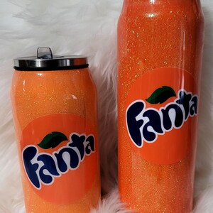 Puede incluir: Dos vasos de glitter naranja con un logotipo de Fanta y un dise&ntilde;o de rodaja de naranja. Los vasos son de diferentes tama&ntilde;os.