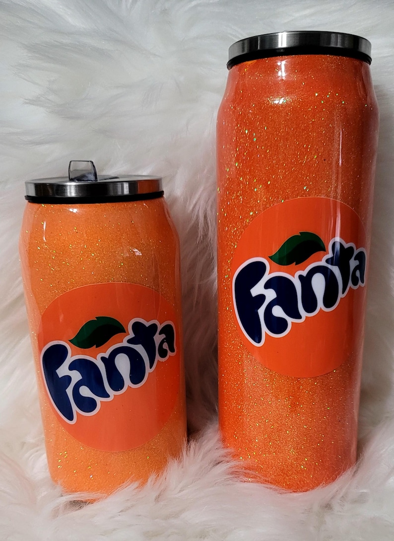 Puede incluir: Dos vasos de glitter naranja con un logotipo de Fanta y un dise&ntilde;o de rodaja de naranja. Los vasos son de diferentes tama&ntilde;os.