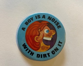 May include: A blue and white button with a cartoon illustration of a person with red hair and the text "A boy is a noise with dirt on it".