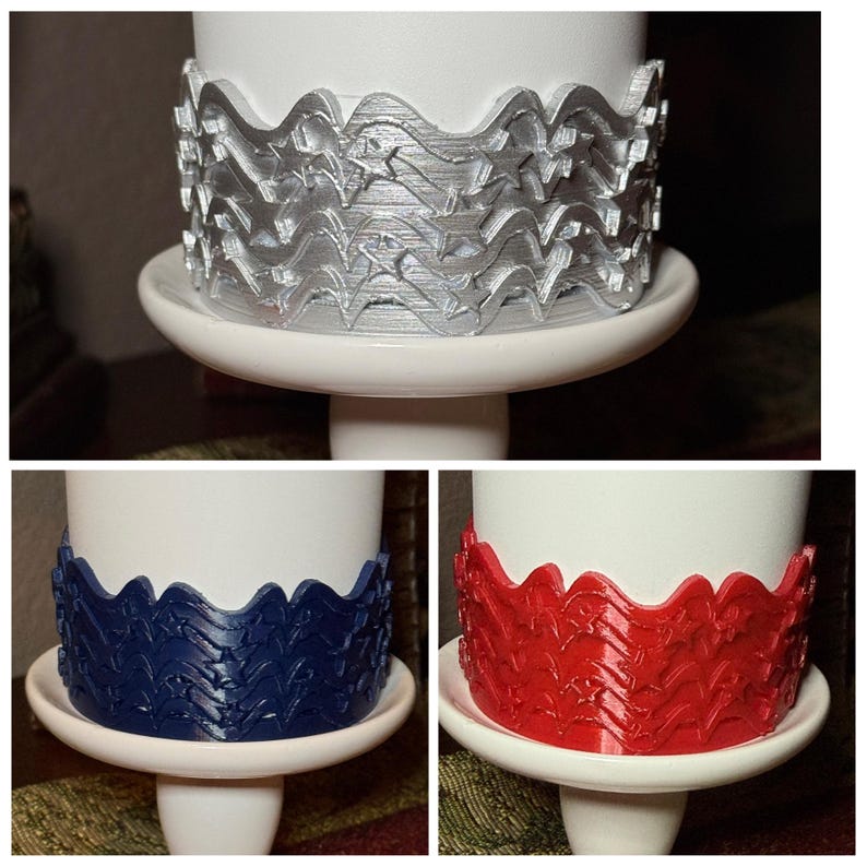 May include: A set of three cylindrical candle wraps featuring a raised, wavy, star-patterned design. The wraps are available in metallic silver, solid navy blue, and solid red, each encircling a plain white candle base on a white pedestal.