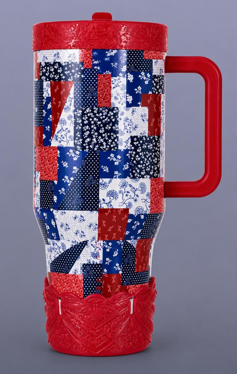 May include: A tall travel mug featuring a patchwork pattern of red, white, and blue squares with various floral, paisley, and polka dot prints. The mug has a solid red lid, a red handle, and a decorative red base with an embossed floral design.