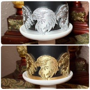 May include: A black candle holder with a silver eagle design. The eagle has its wings spread and is centered on the holder. The candle holder sits on a white base. A second image shows the same candle holder with a gold eagle design.
