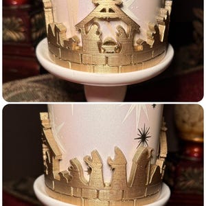 May include: A decorative candle holder featuring a gold-coloured nativity scene and starburst design. The candle holder is white and has a gold-coloured decorative border. The candle holder is on a white pedestal.