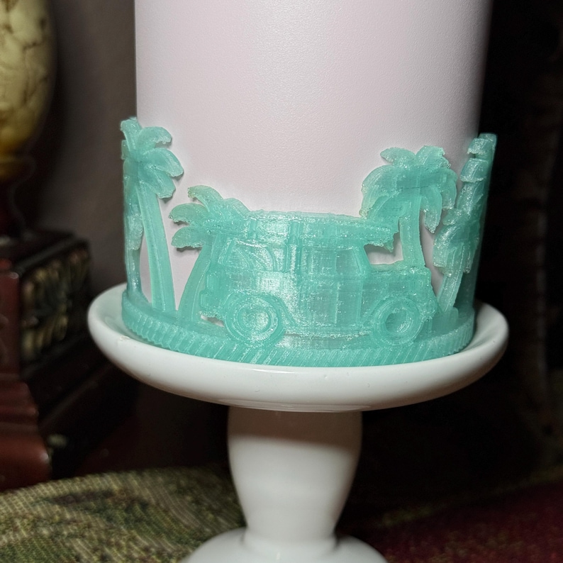 May include: A light pink cylindrical container featuring a wrap-around mint green 3D-printed decorative band. The band displays a repeating relief pattern of palm trees and a vintage-style van, all resting on a white pedestal stand.