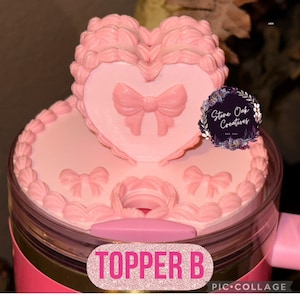 May include: A pink tumbler topper with a heart-shaped design and bow accents. The topper features the text "TOPPER B" in a glittery font. The design includes a decorative border and a logo that says "Stone Oak Creatives".