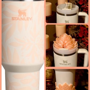 May include: A white stainless steel travel mug with a pink floral pattern and a pink lid. The mug has the Stanley logo on the front. The mug is shown with a pink flower-shaped lid topper.