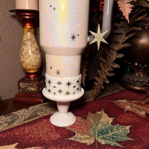 May include: A white ceramic mug with a black handle and the text "But First, Coffee" in a black, handwritten-style font. The mug is on a white surface.